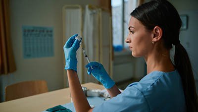 Медицинский работник набирает в шприц раствор для введения